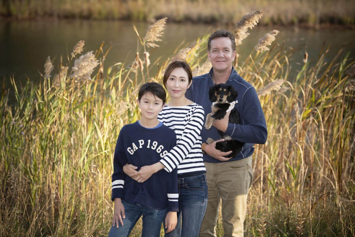 a family of three standing outdoor in front of a natural lake with their dog