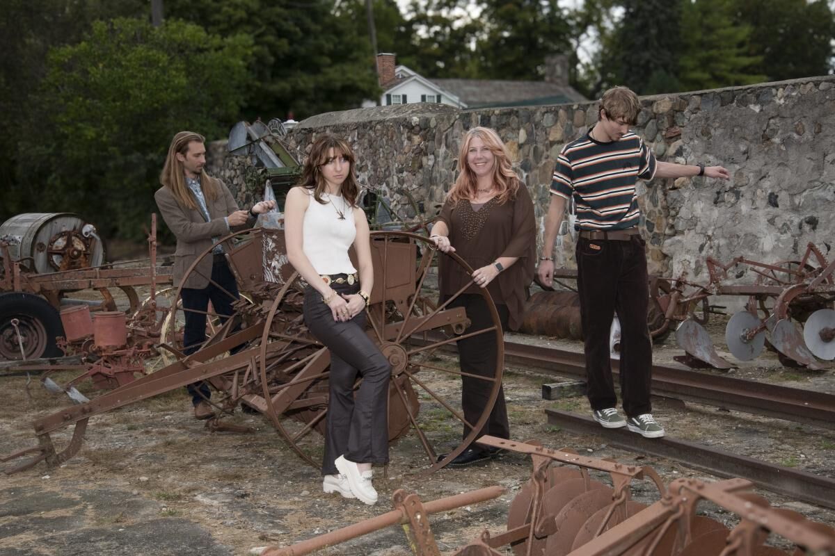 A family with two women and two men staying on an old farm equipment with stone wall on the background