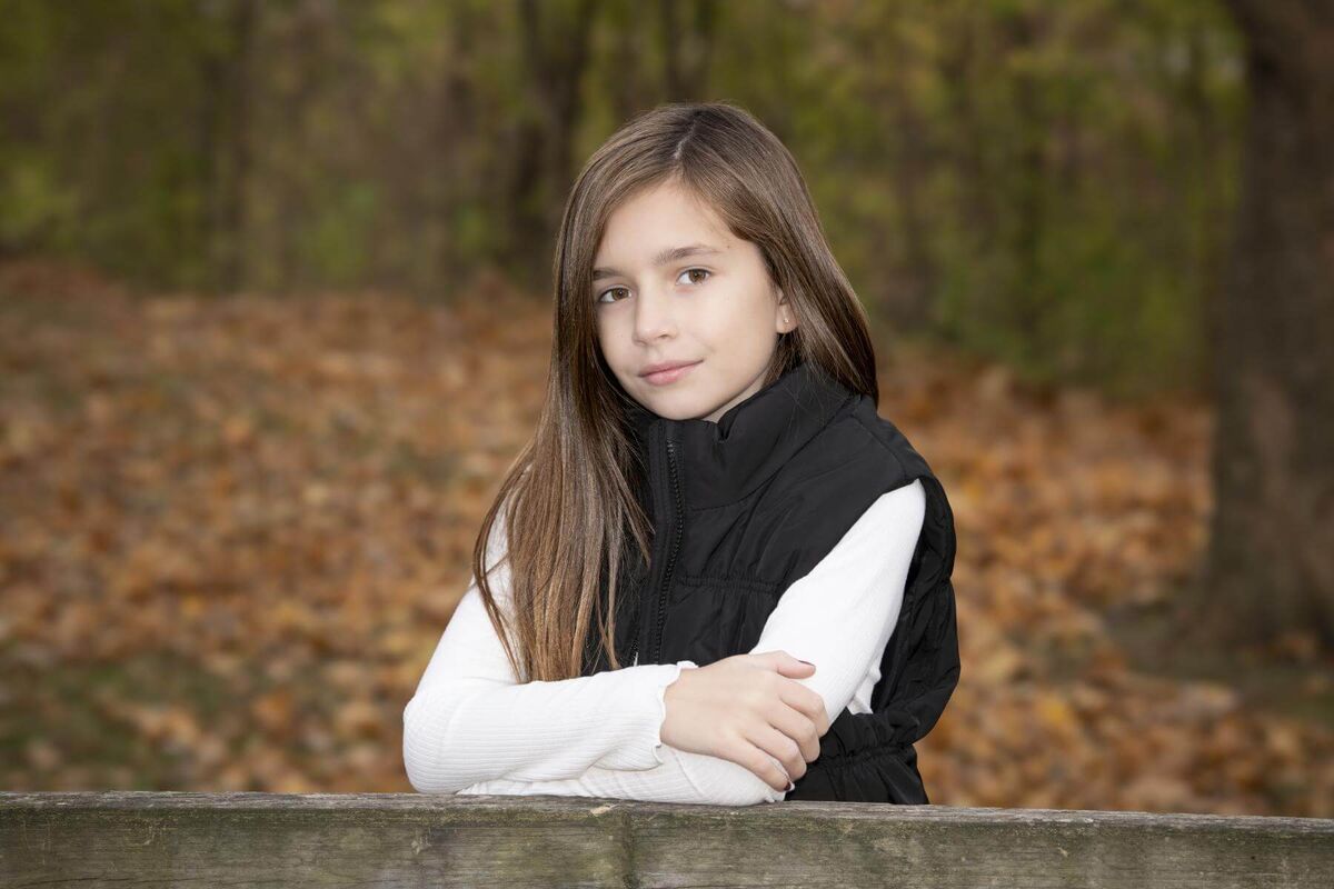 girl with long hair staying behind park bench in a white sweatshirt and black vest