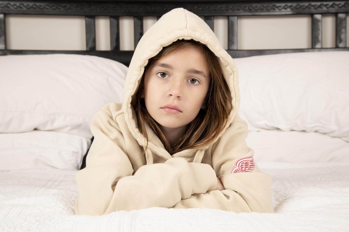 kid portrait of a girl in a milk color hoodie laying on a king bed